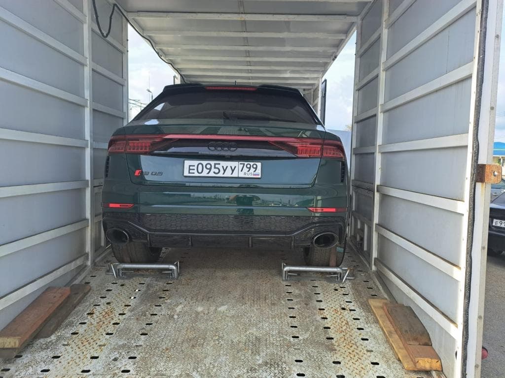 Тёмно-зелёная Audi RS Q8 в закрытом кузове автовоза, вид сзади: упоры за задними колёсами, перфорированный пол