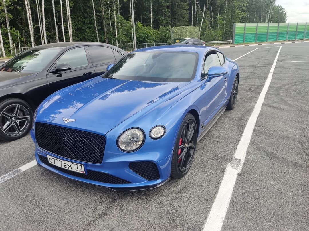 Синий Bentley Continental GT и чёрный Mercedes на асфальтовой площадке у леса перед перевозкой