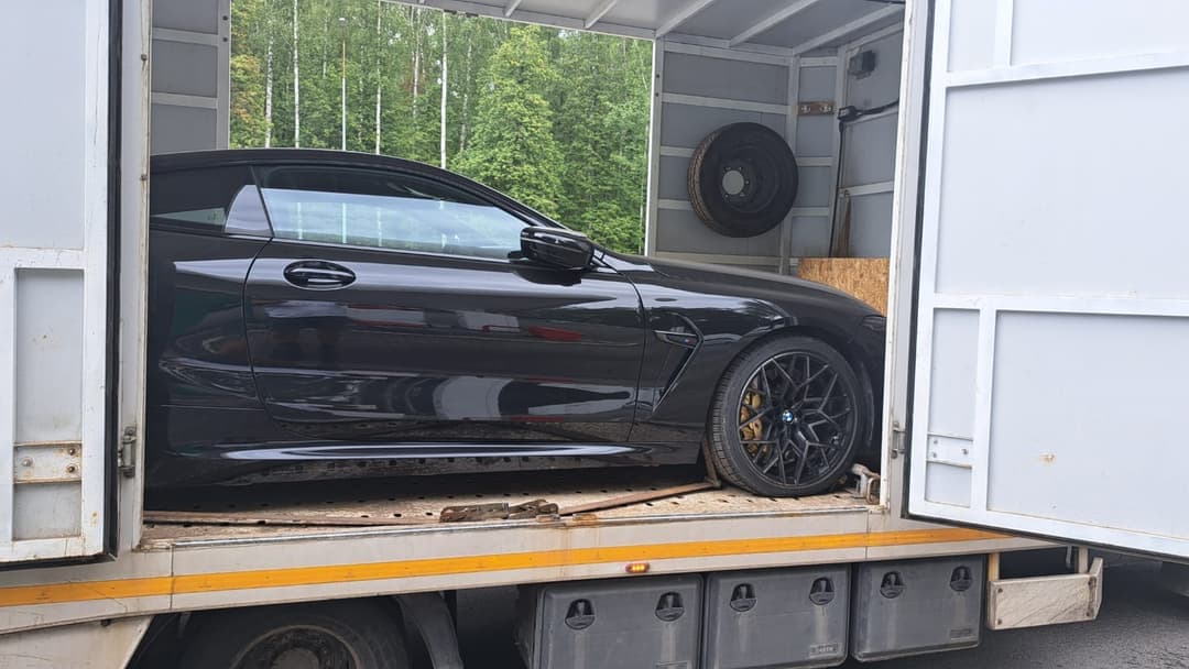 BMW M8 inside an enclosed transporter, viewed from the side